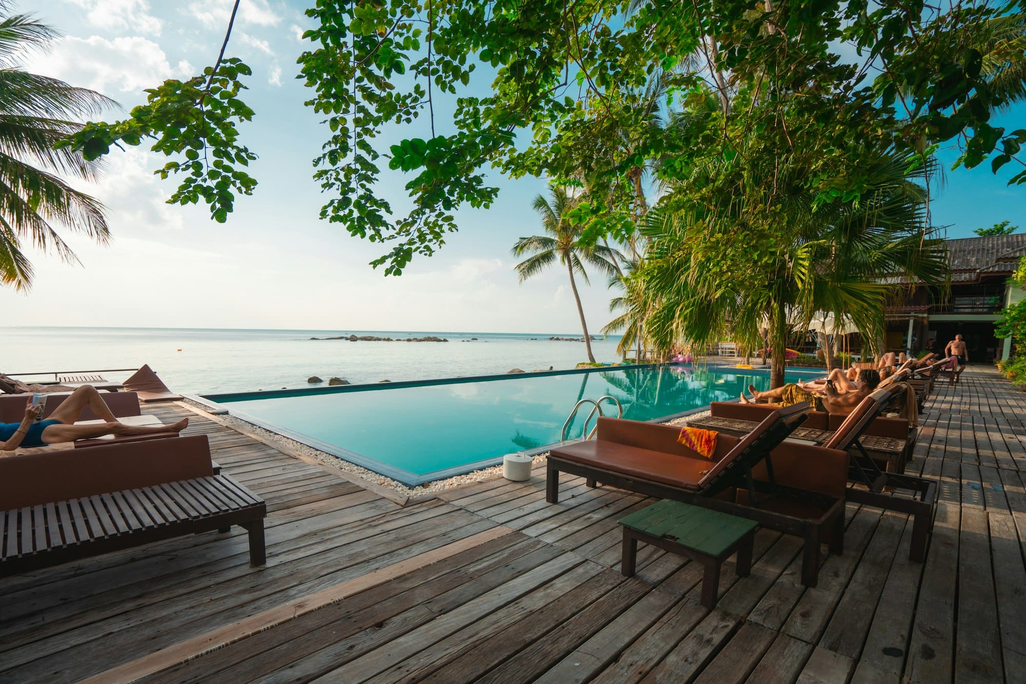 A teak pool deck with sun loungers beneath tropical trees