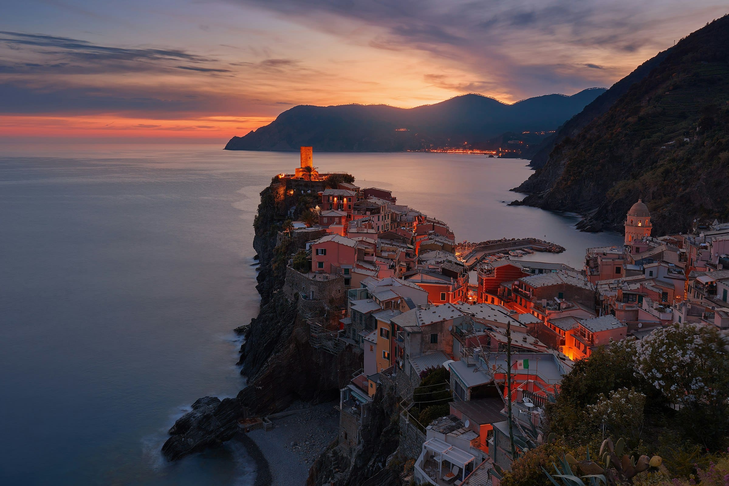 A cliffside coastal village glowing at dusk above the sea