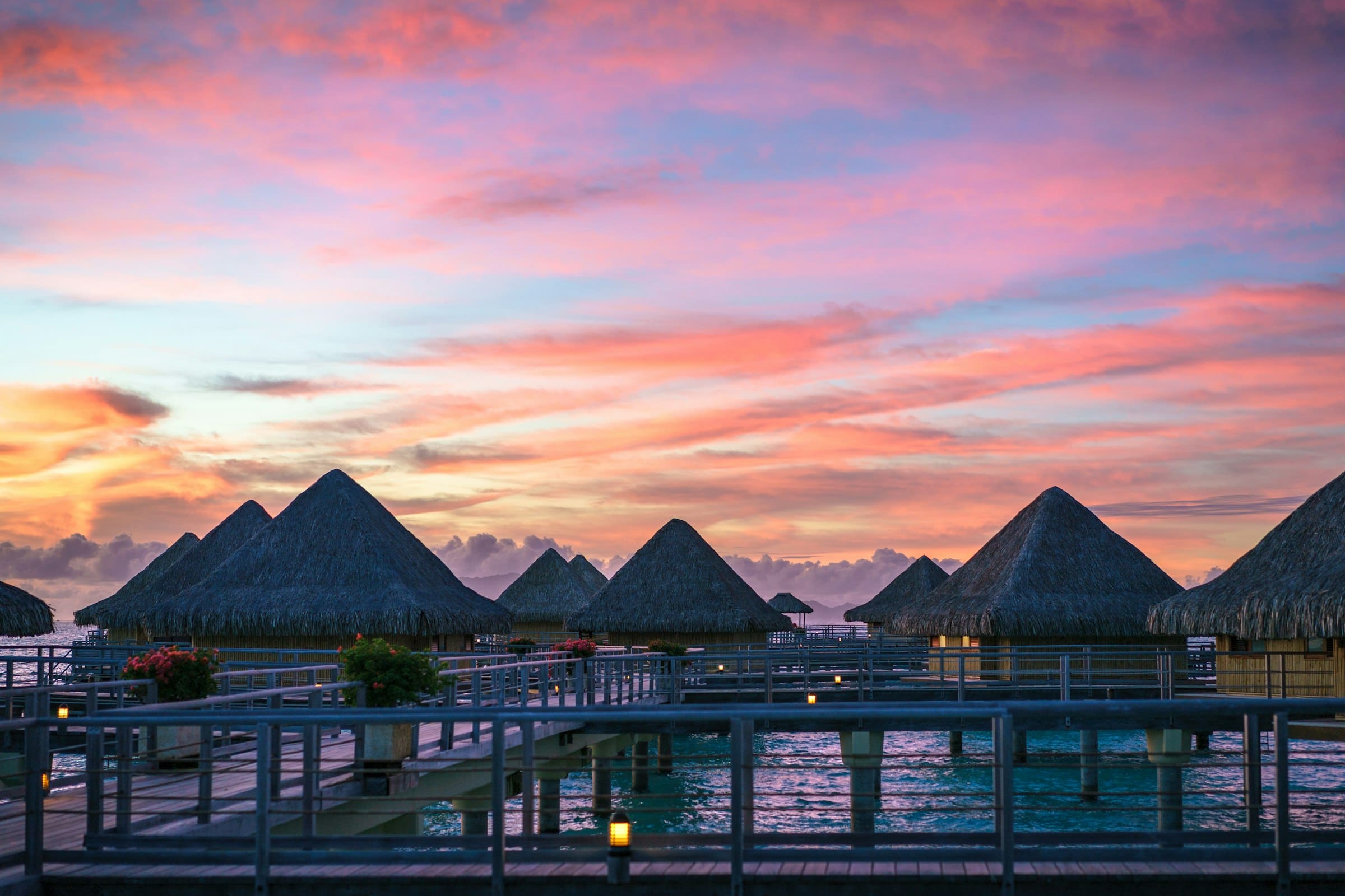 Overwater villas silhouetted against a pink and orange sunset