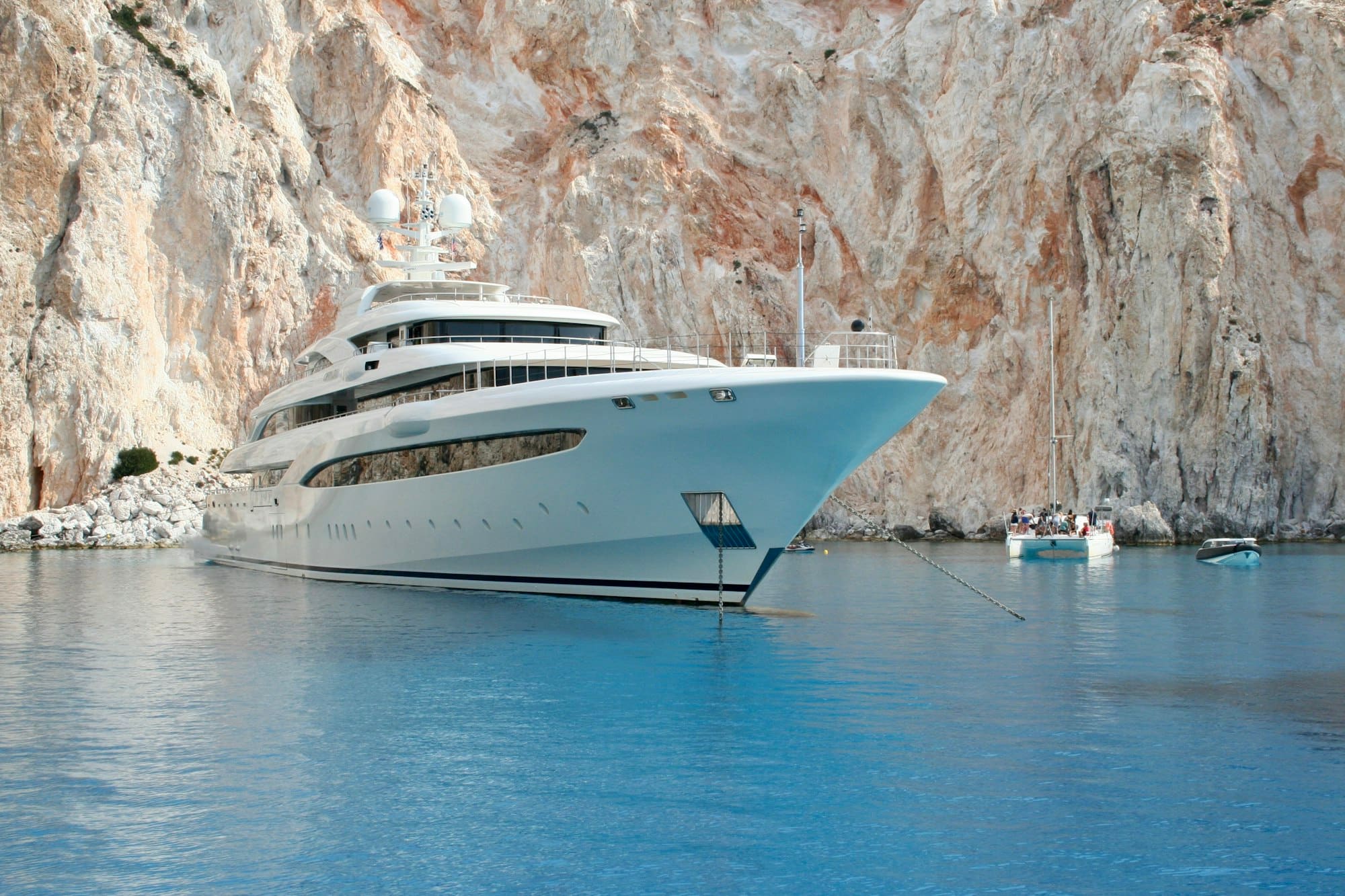 A white superyacht anchored beneath limestone cliffs in clear turquoise water